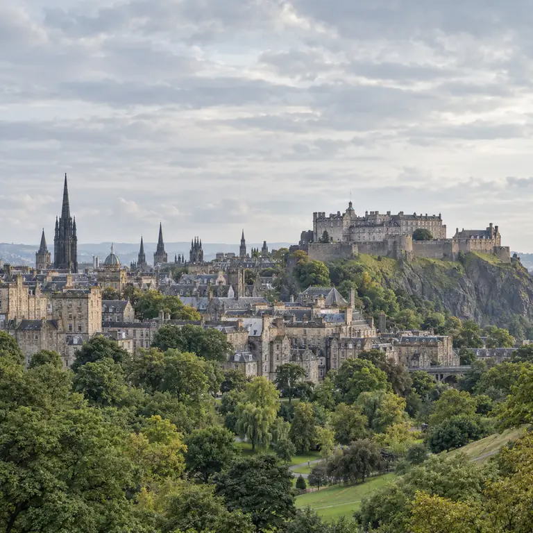 Edinburgh Kalesi ve Eski Şehir silueti, bulutlu gökyüzünün altında yeşil bahçelerin üzerinde yükseliyor.