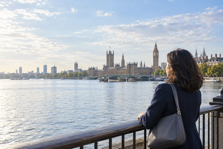 Lacivert paltolu bir kadın Thames kıyısından Westminster Köprüsü ve Elizabeth Kulesi yönüne bakıyor.